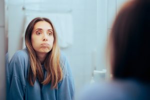 Woman looking in the mirror with a stressed look on her face.