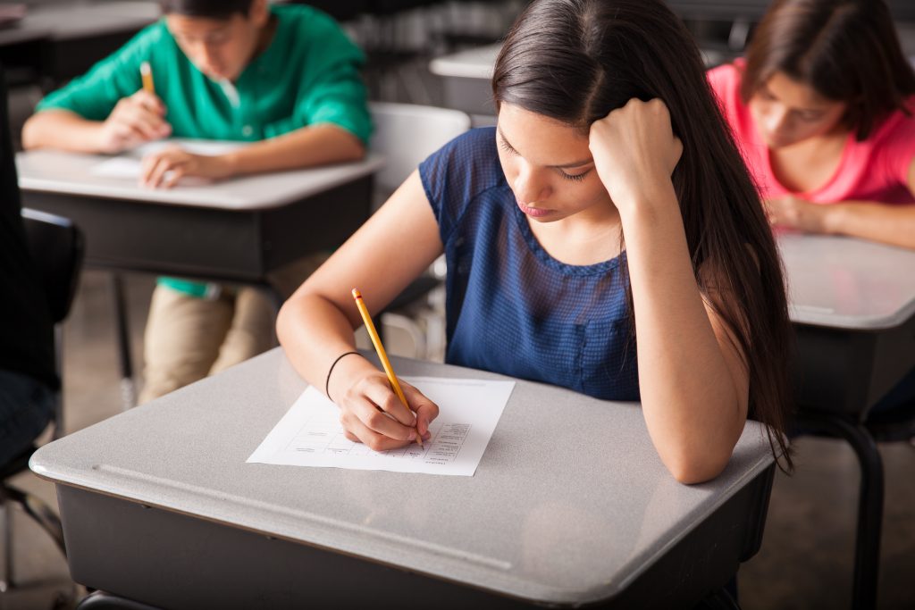 Girl at a desk with one hand on her head and the other hand writing.